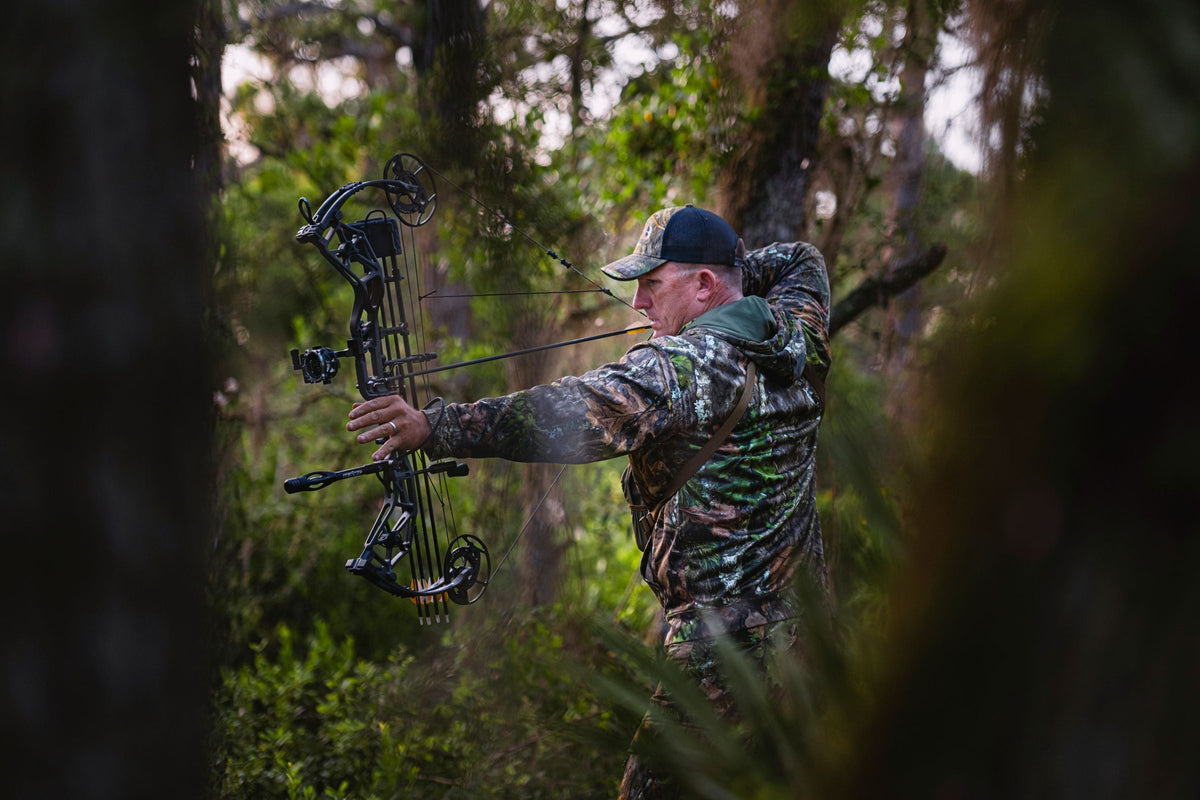 Bowhunter in camo drawing a Bear compound bow in a green forest