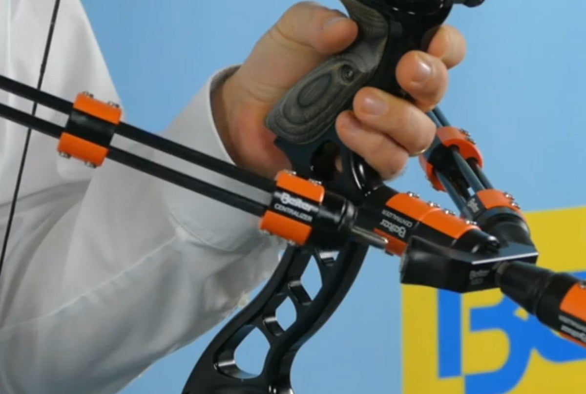 Archer's hand on a recurve riser fitted with orange Beiter Centralizer stabilizer mounts