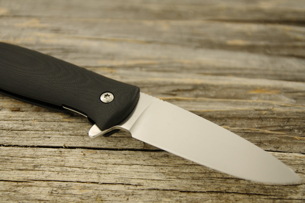 North Arm Knives Skaha II folding knife with black G10 handle, open on weathered wood
